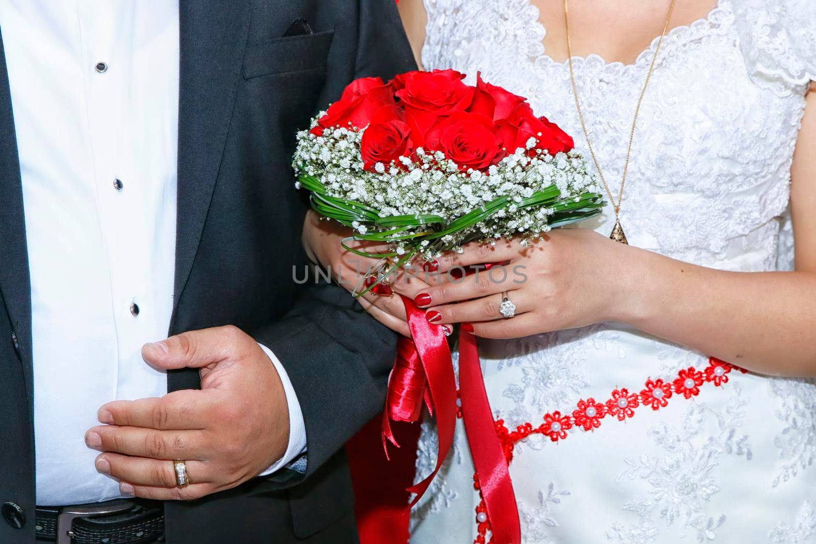 Bride holding colorful flowers bouquet with her hands on wedding day . The guy and the girl in a white dress standing and holding in her hands a bouquet of red, white flowers and greenery