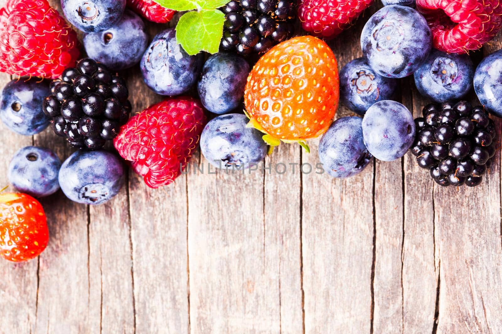 Summer wild berries over shabby wooden background. Raspberry, strawberry, blackberry and blueberry on the table