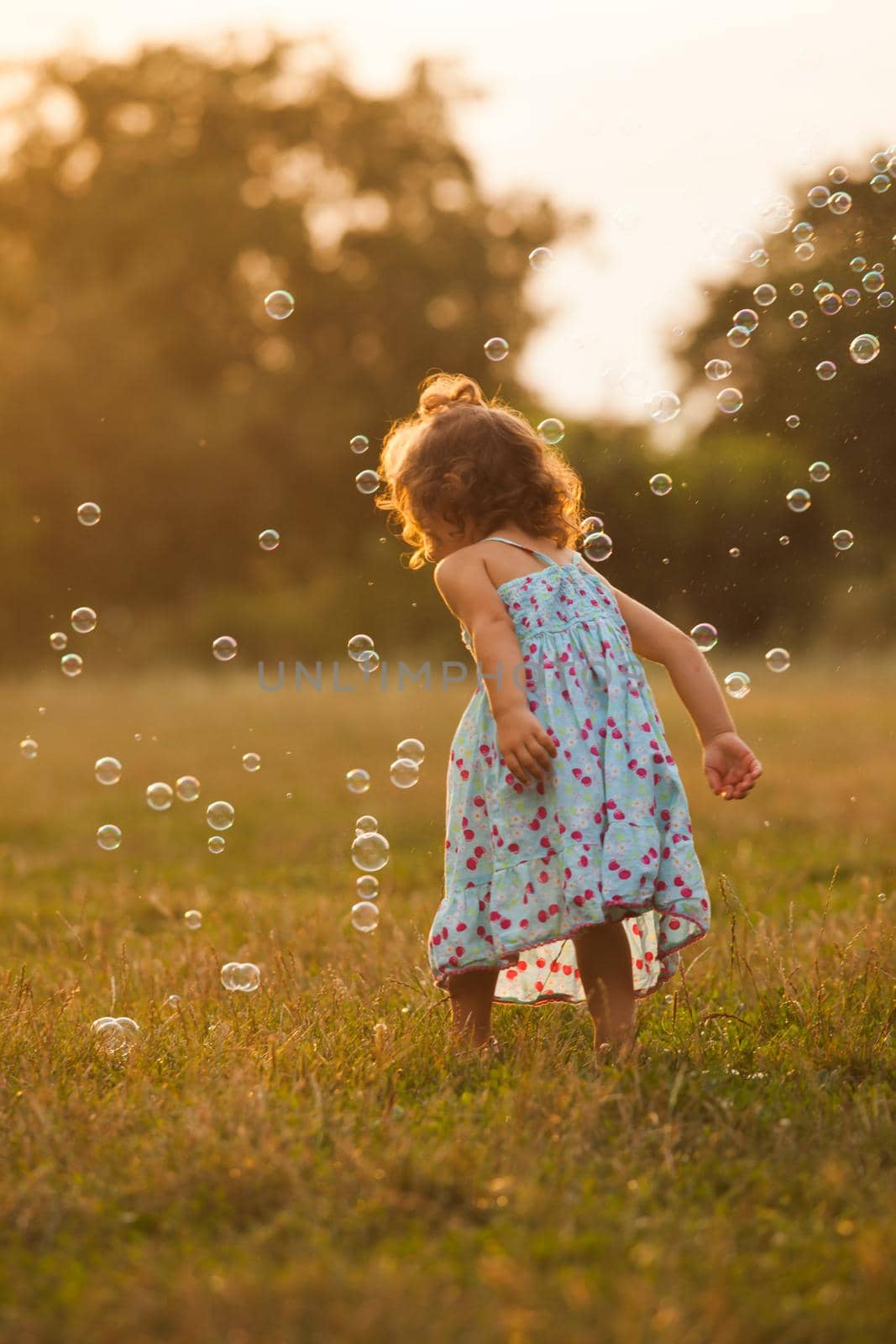 Pretty girl runs for the bubbles in the park on the sunset