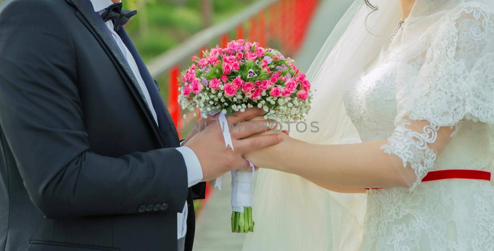 They held the pink flower bouquet in their hands . hands folded behind their back, hold a beautiful little wedding bouquet of roses . The newlyweds hold in their hands a wedding bouquet between each other. by Adil_Celebiyev_Stok_Photo