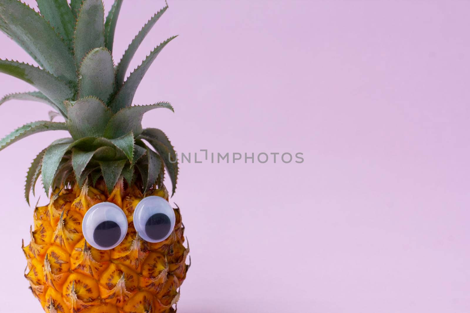 Closeup of fresh pineapple with green leaves and googly eyes on pink background, by uveita