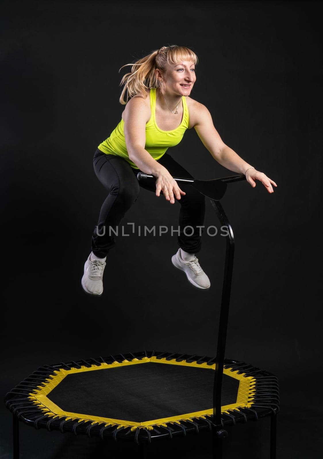 Girl on a fitness trampoline on a black background in a yellow t-shirt gym sport, equipment girl leap, cute elastic muscle instructor enjoy