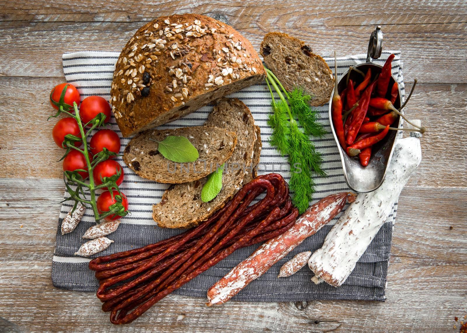 Wholemeal bread with dried salami sausages, tomatoes, greens, chili pepper on a wooden rustic table