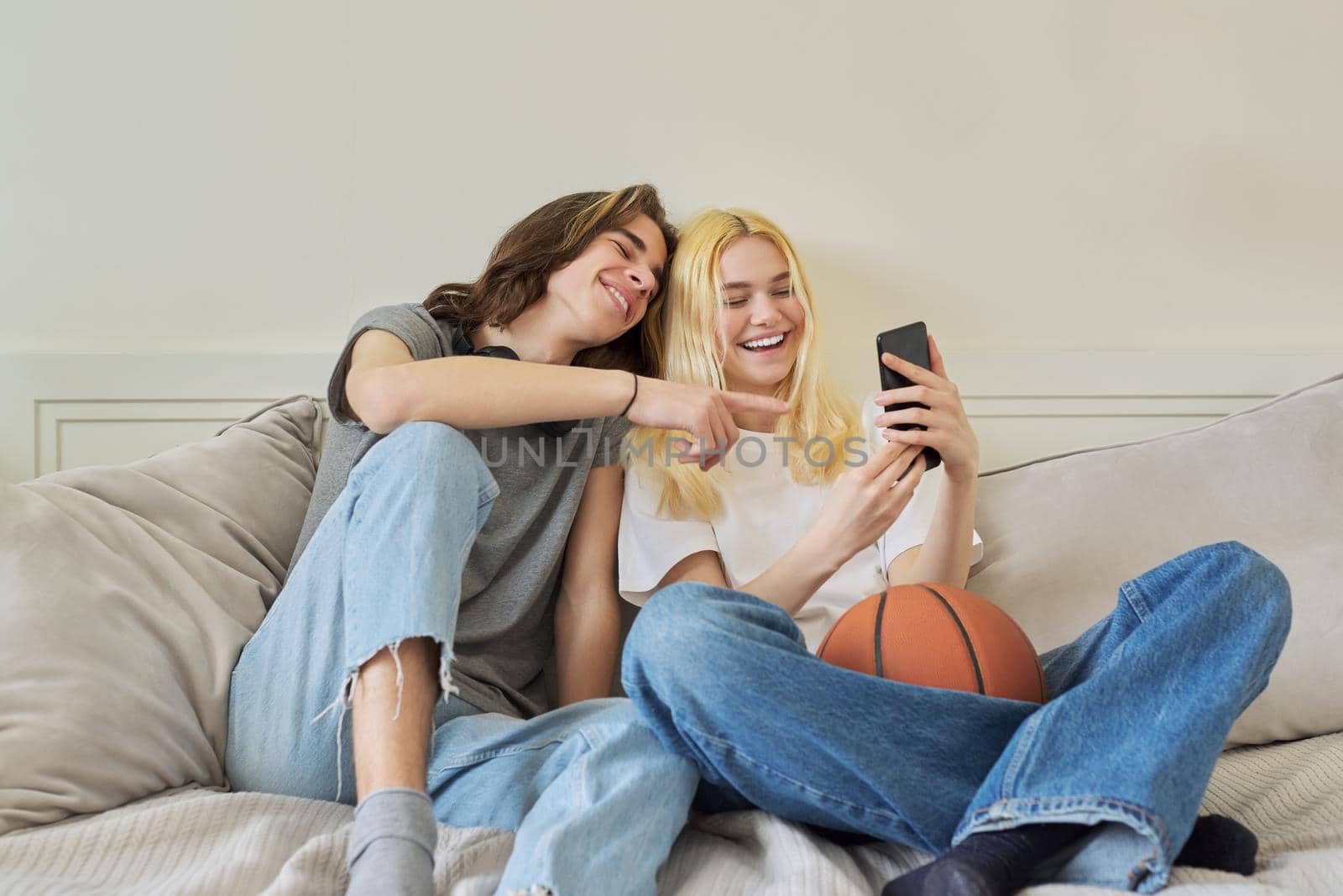 Happy laughing hipster teenagers male and female having fun using smartphone together. Couple takes photos chat online using video call. Lifestyle, technology, friendship, communication of adolescents