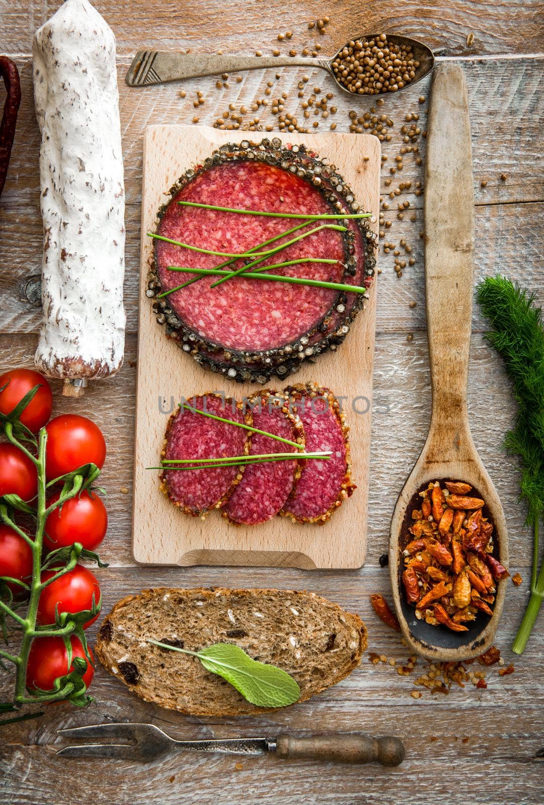 Dried sausage with cherry tomatoes, bread, greens and chili on a wooden table