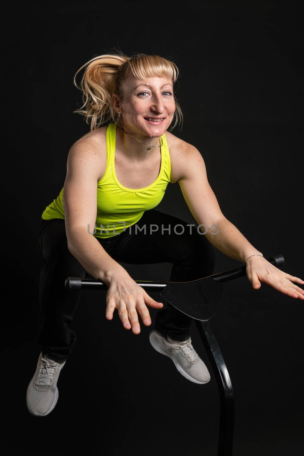 Girl on a fitness trampoline on a black background in a yellow t-shirt energy woman, fun exercise female leap, cute young muscle instructor enjoy by 89167702191