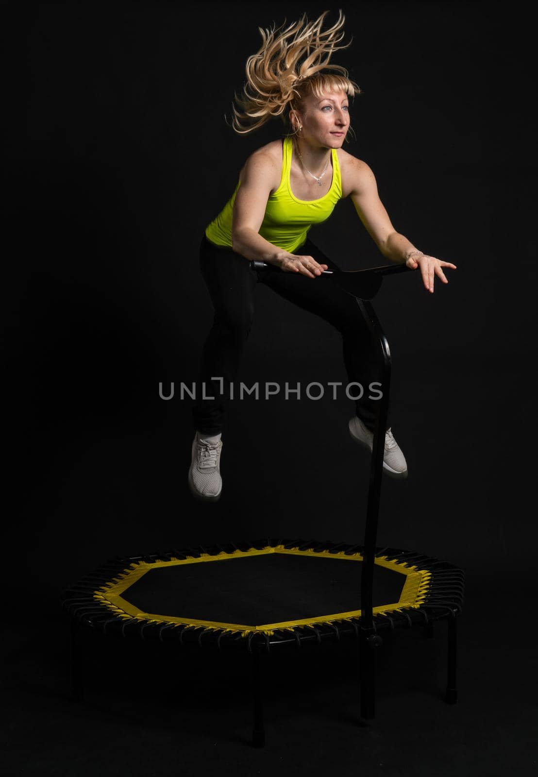 Girl on a fitness trampoline on a black background in a yellow t-shirt trampoline fit sport, exercise athlete healthy cardio, workout Fly center motion, physical muscle instructor enjoy by 89167702191