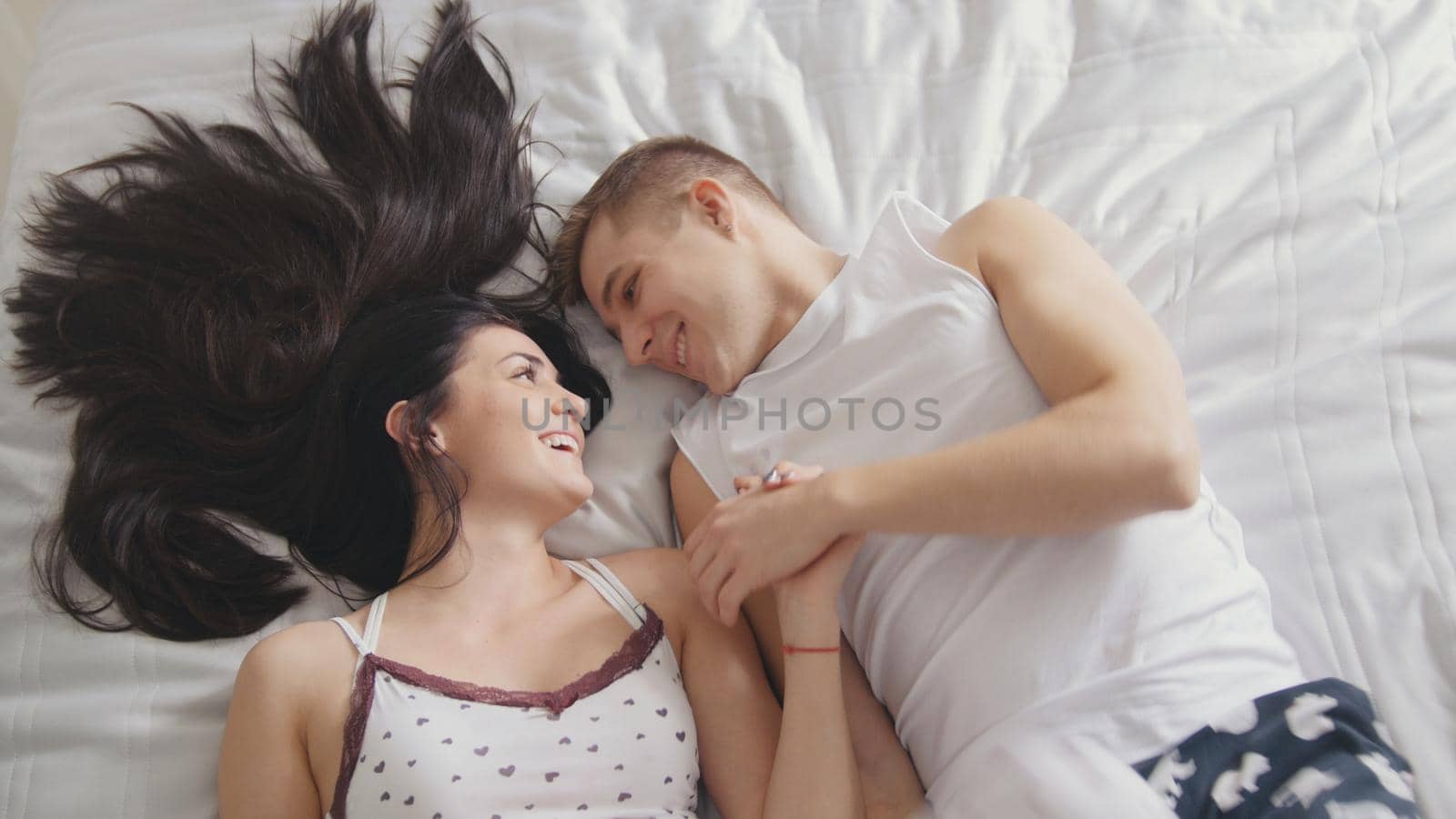 Happy loving couple in bed, smiling and touching each other, view from top, close up