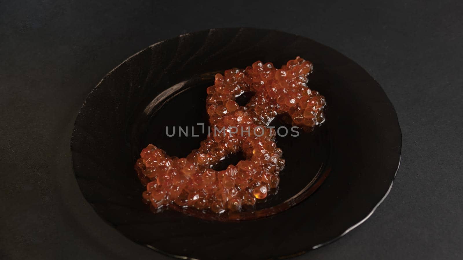 The symbol of a dollar of delicacy real red caviar on a glass black plate on a gray background is a view from above. Food in the world's elite restaurants is a symbol of money