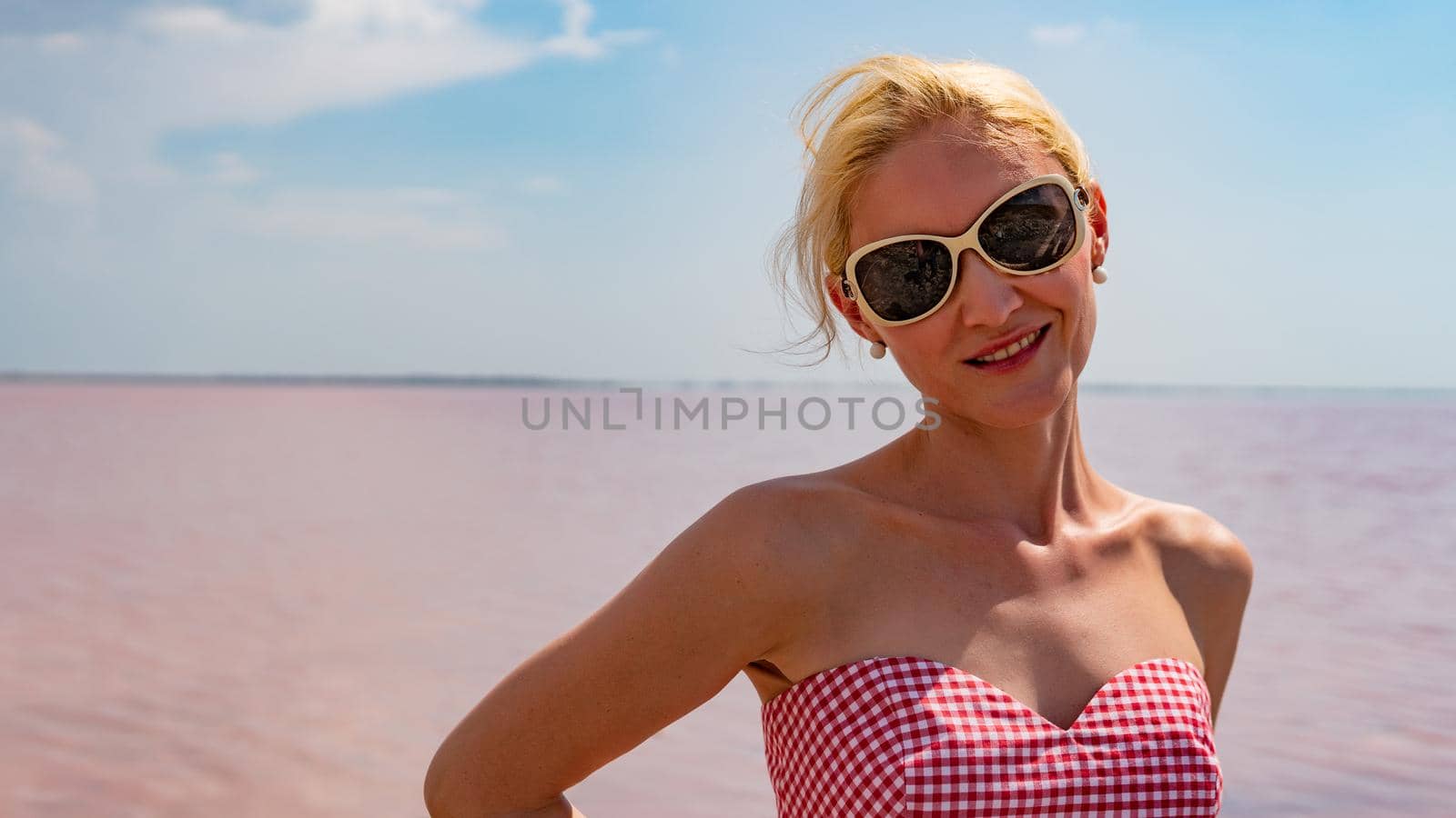 Cheerful woman in a beautiful dress young with beautiful eyes on the background of a red lake during the day and in summer