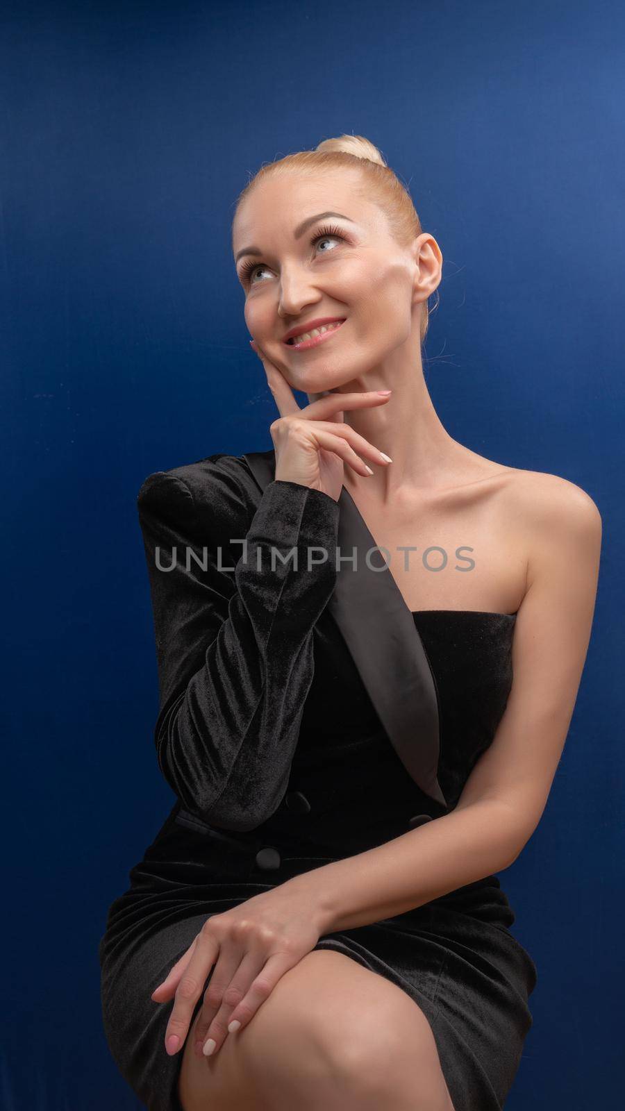 A nice mature girl sits on a chair, lovely in a black suit with a European face background in purple white daylight. Make up by 89167702191