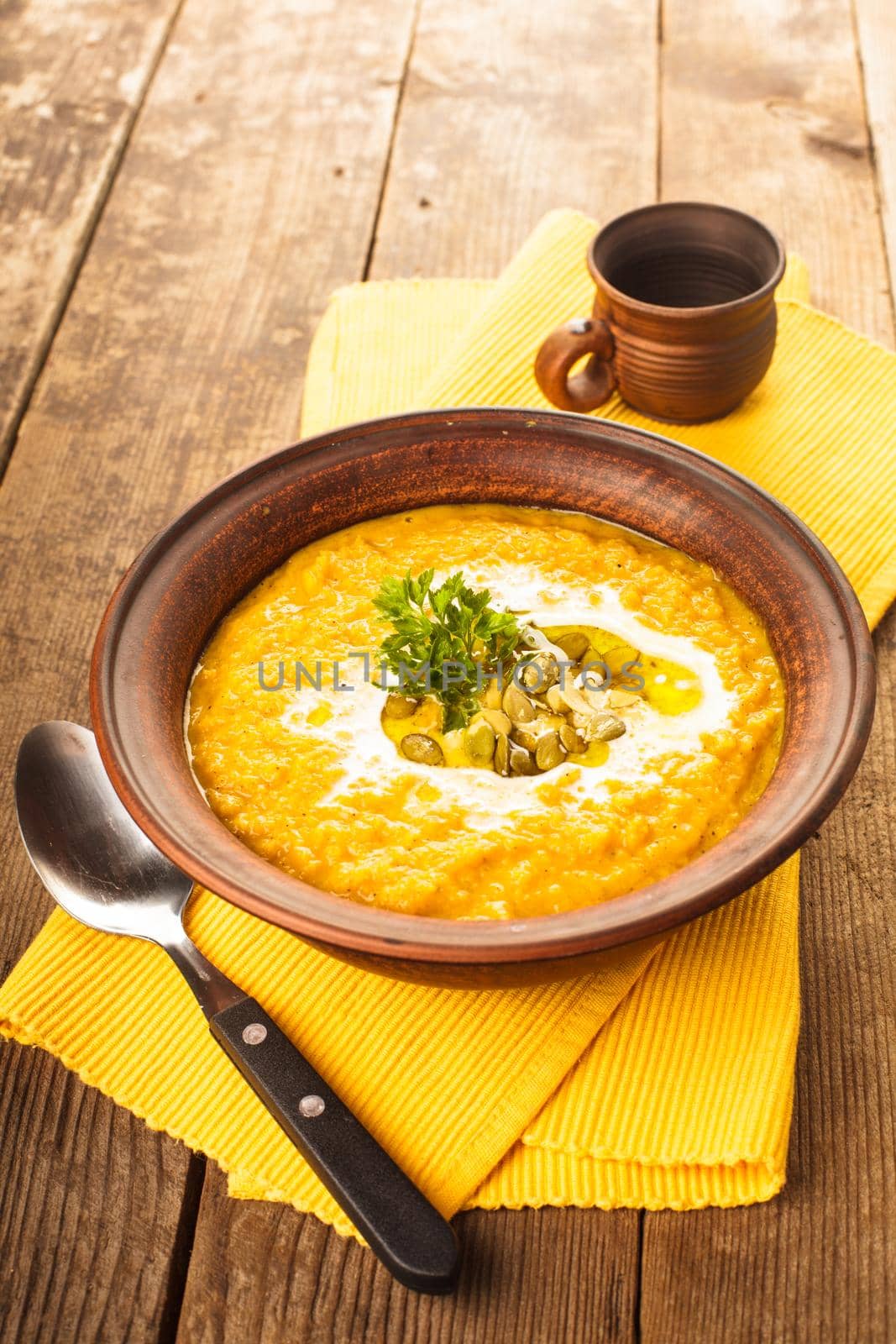 Pumpkin soup in clay bowl with spoon on the table