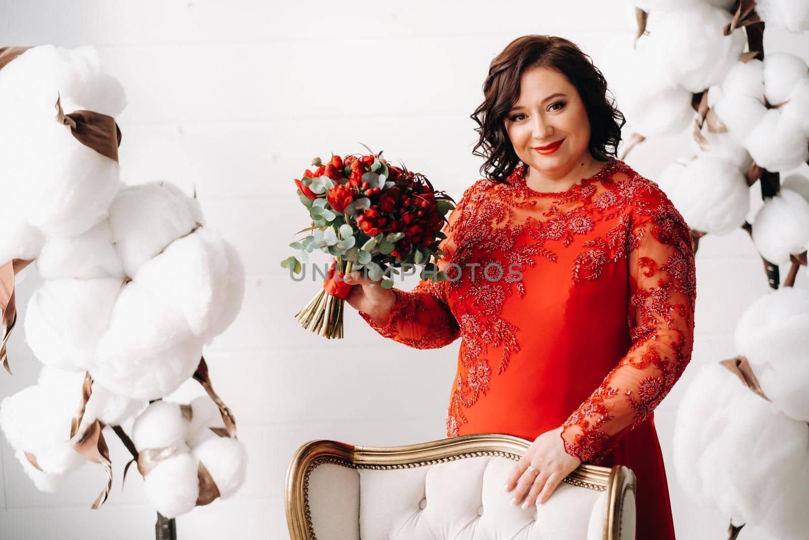 a woman in a red dress stands and holds a bouquet of red roses and strawberries in the interior. by Lobachad