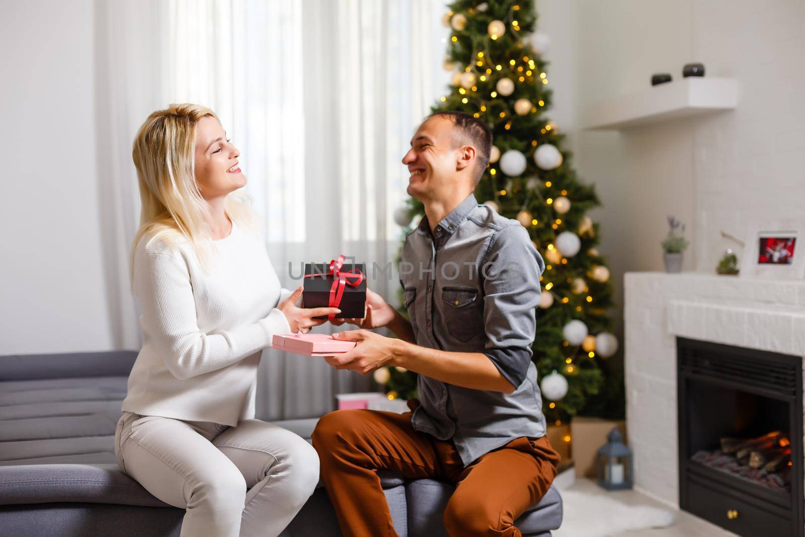 Happy young people give each other gifts by the fireplace near the Christmas tree.