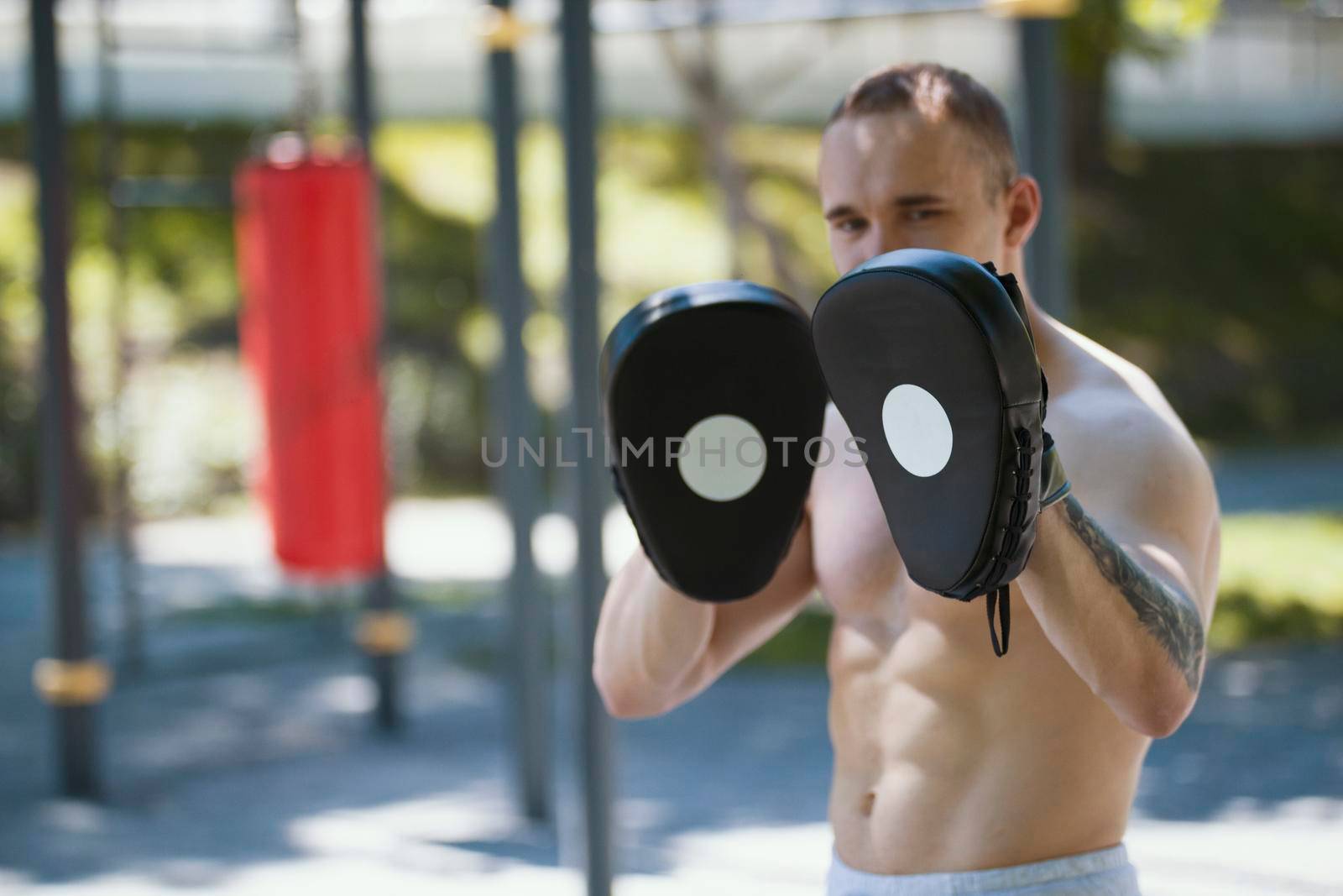 Muscular man boxer in boxing paws, workout in summer park, horizontal