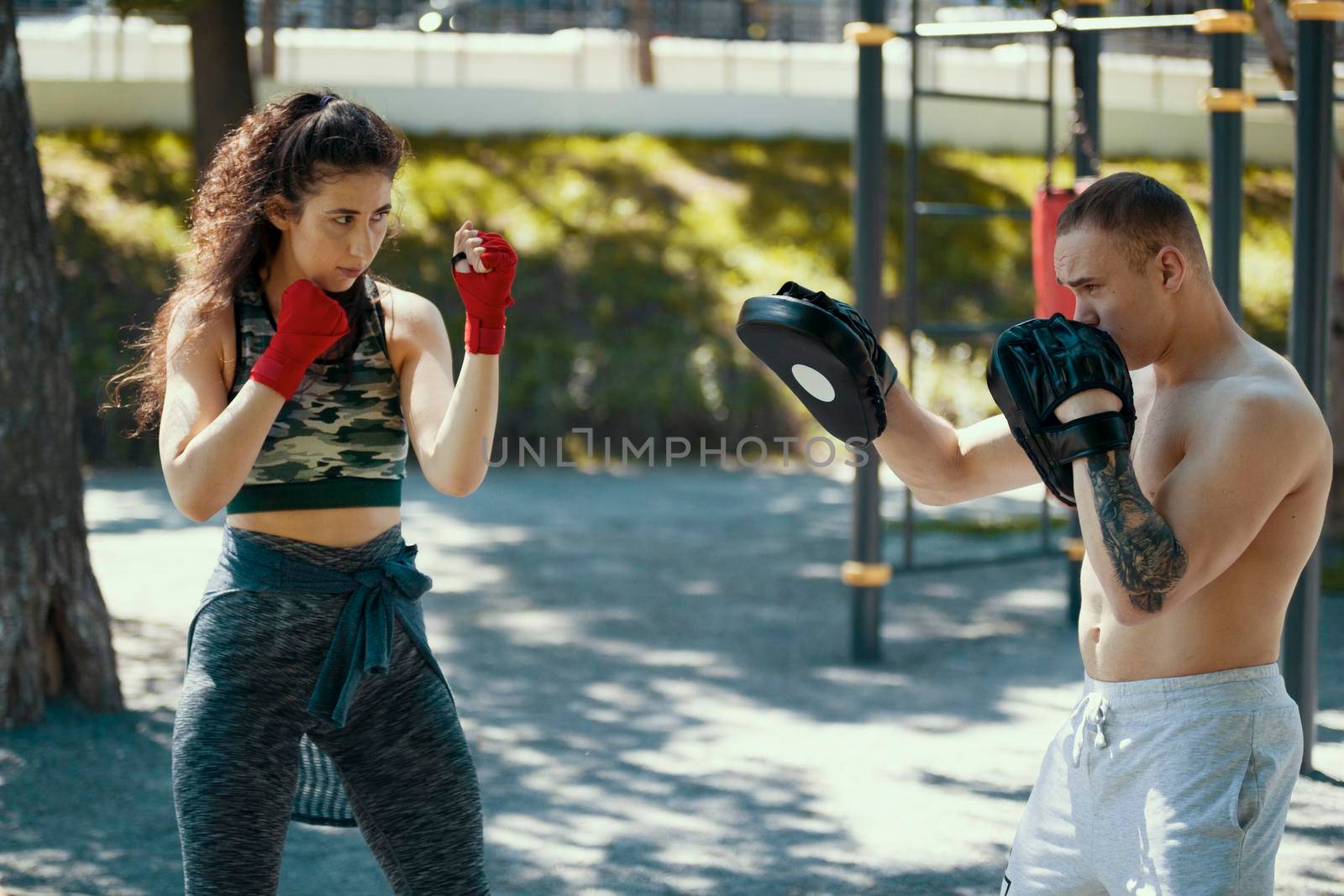 Boxers - muscular man and young woman engaged in boxing in the park ar sunny day, horizontal