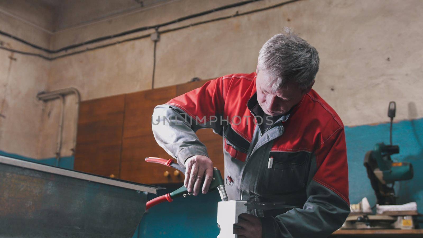 Worker assembling the metal part by hand with pliers, tools for grinding metal and metal details in the foreground, industrial concept