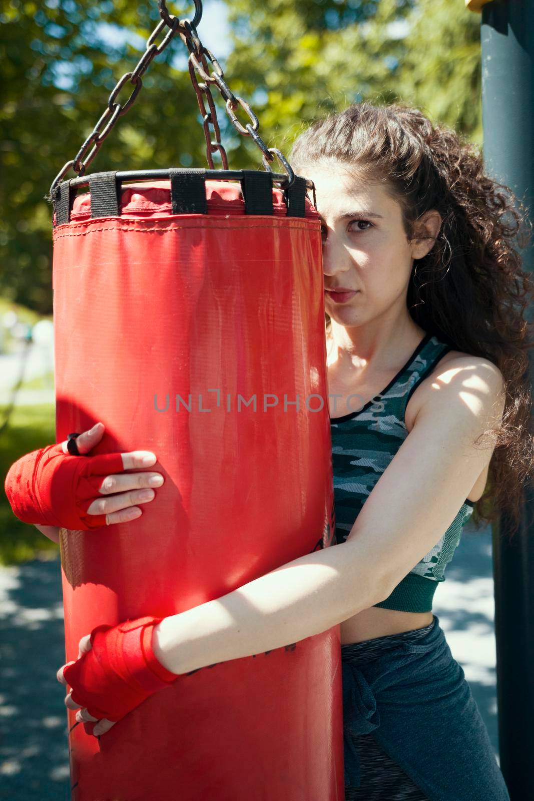 Portrait of sportive woman in sportswear hugging the punching bag, close up