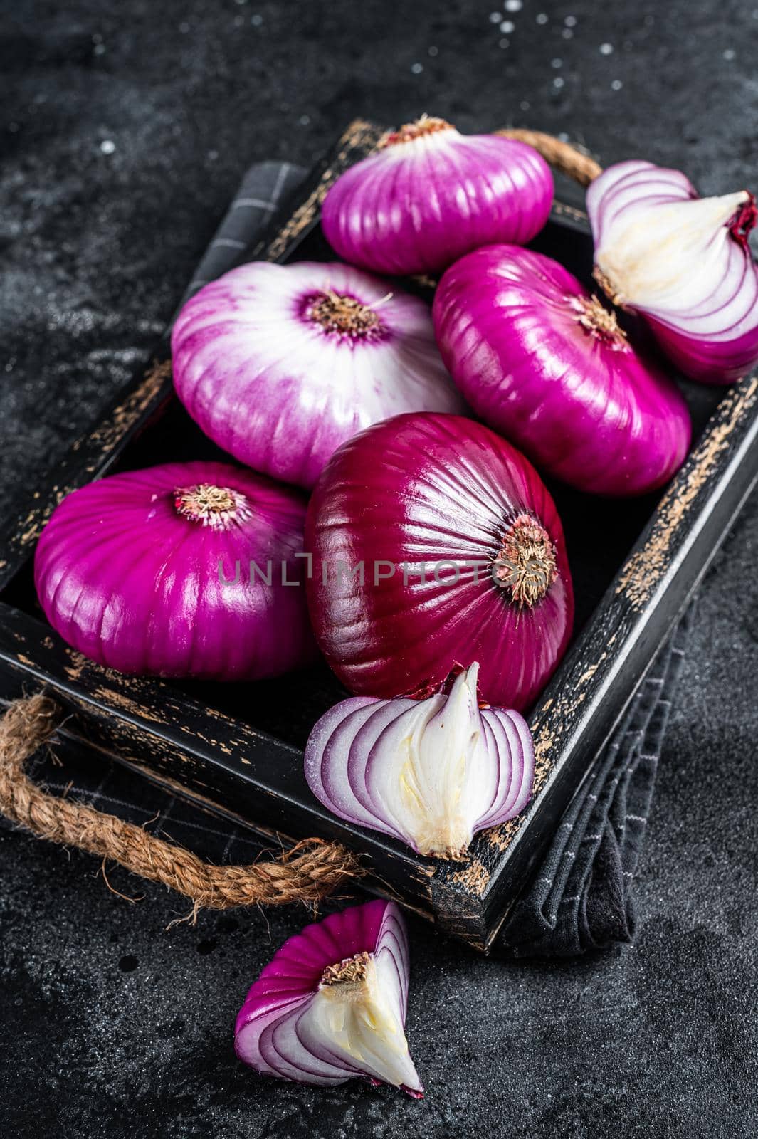 Flat red sweet onion in a wooden tray. Black background. Top View.