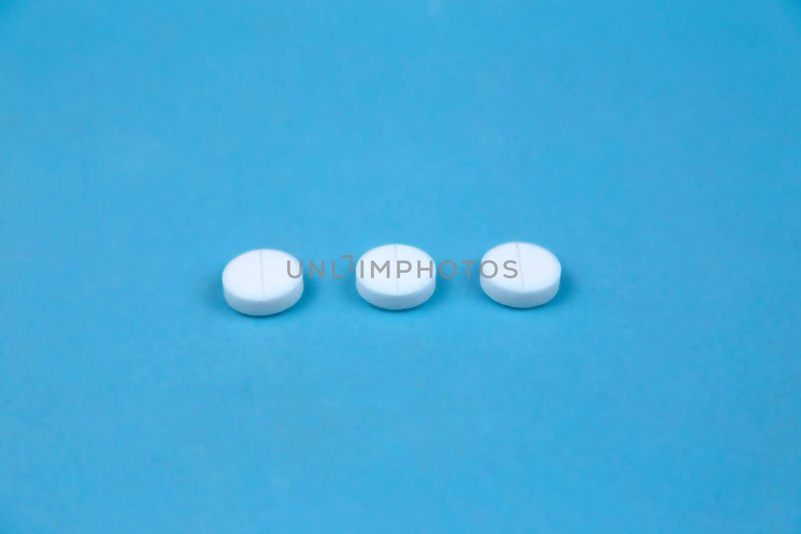 Three white round pills on blue background. Concept of healthcare and medicine communication