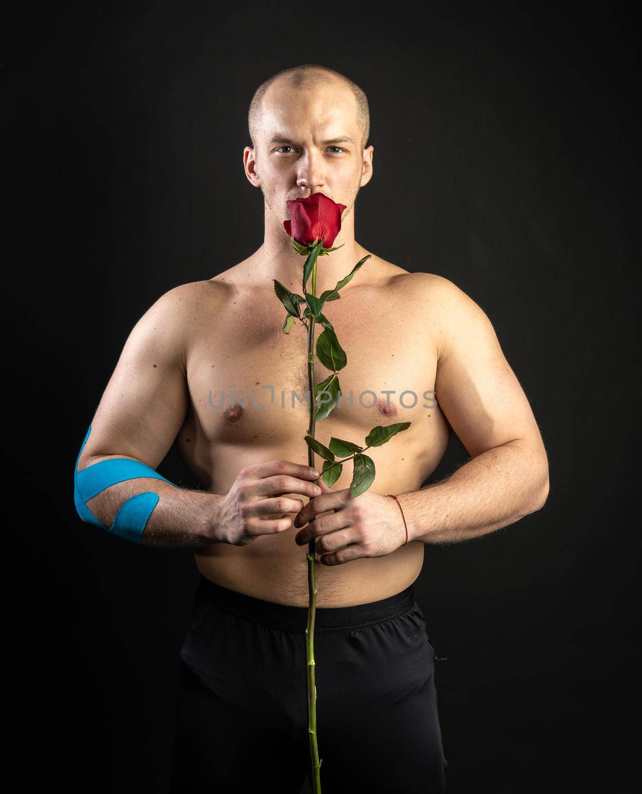Athletic man holding a red rose, naked for the day of velentin pumped up, on his arm a teip bodybuilder romantic. lover guy LGBT. In the studio on a black background Cheerful with beautiful eyes by 89167702191