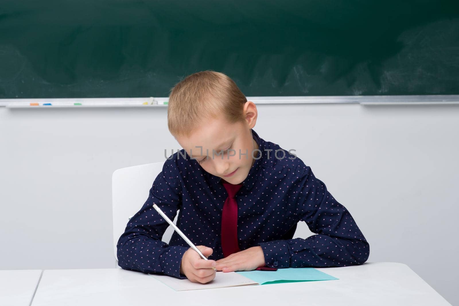 Schoolboy writes in a notebook sitting at a desk by kolesnikov_studio