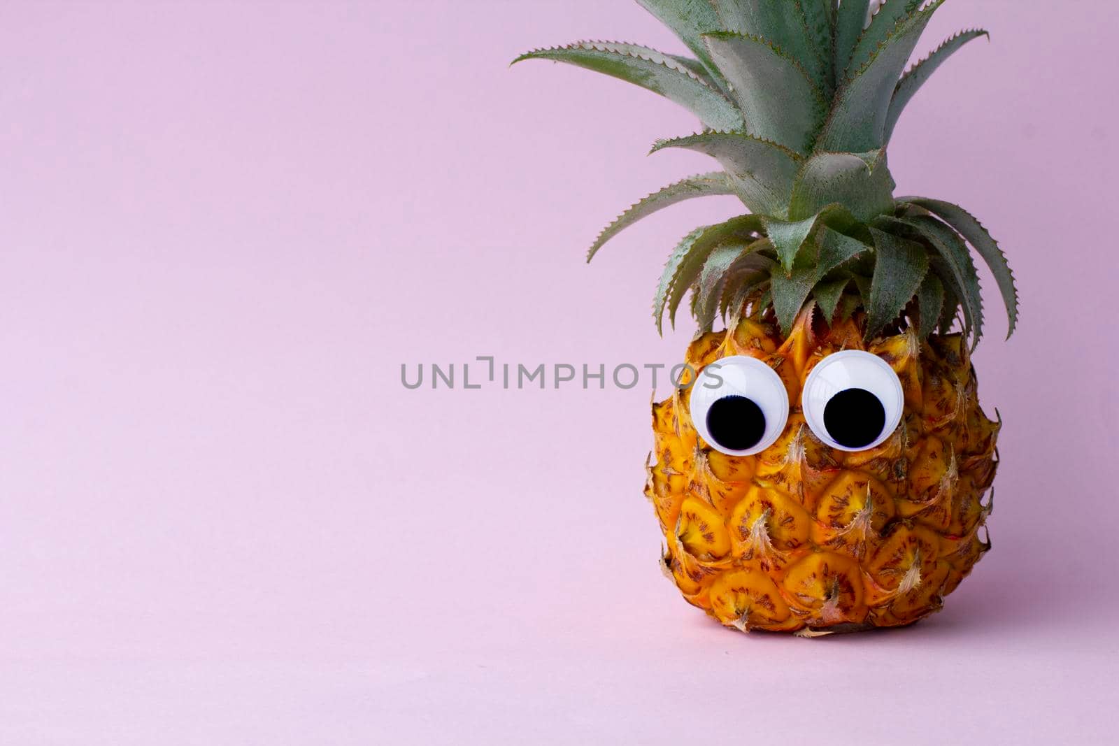 Funny exotic pineapple with googly eyes on pink background by uveita