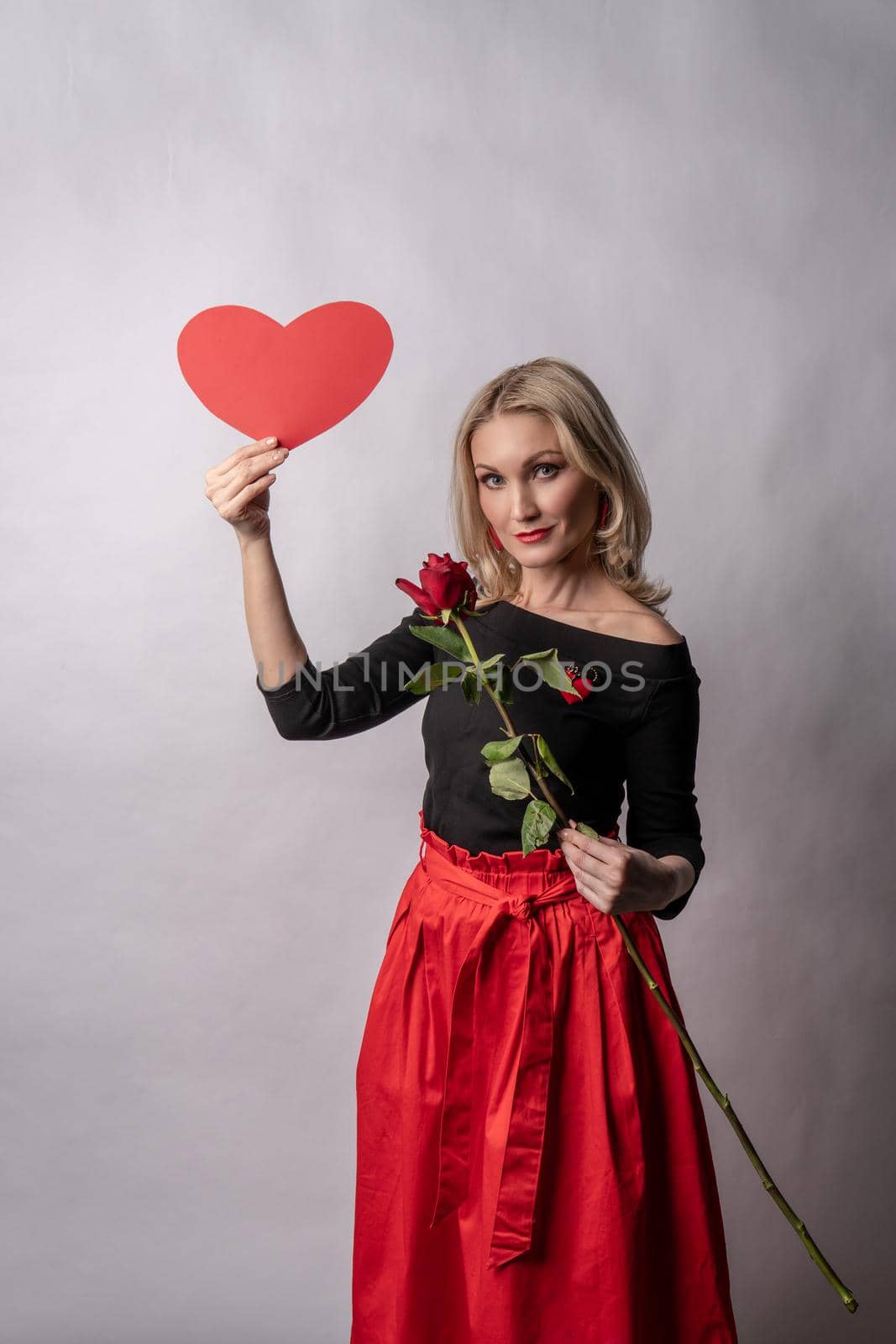 Girl holding rose and heart valentine background, valentine board, on the floor hearts lovely wedding. February 14 honeymoon. emotions festive, engagement in a red dress girl, barefoot