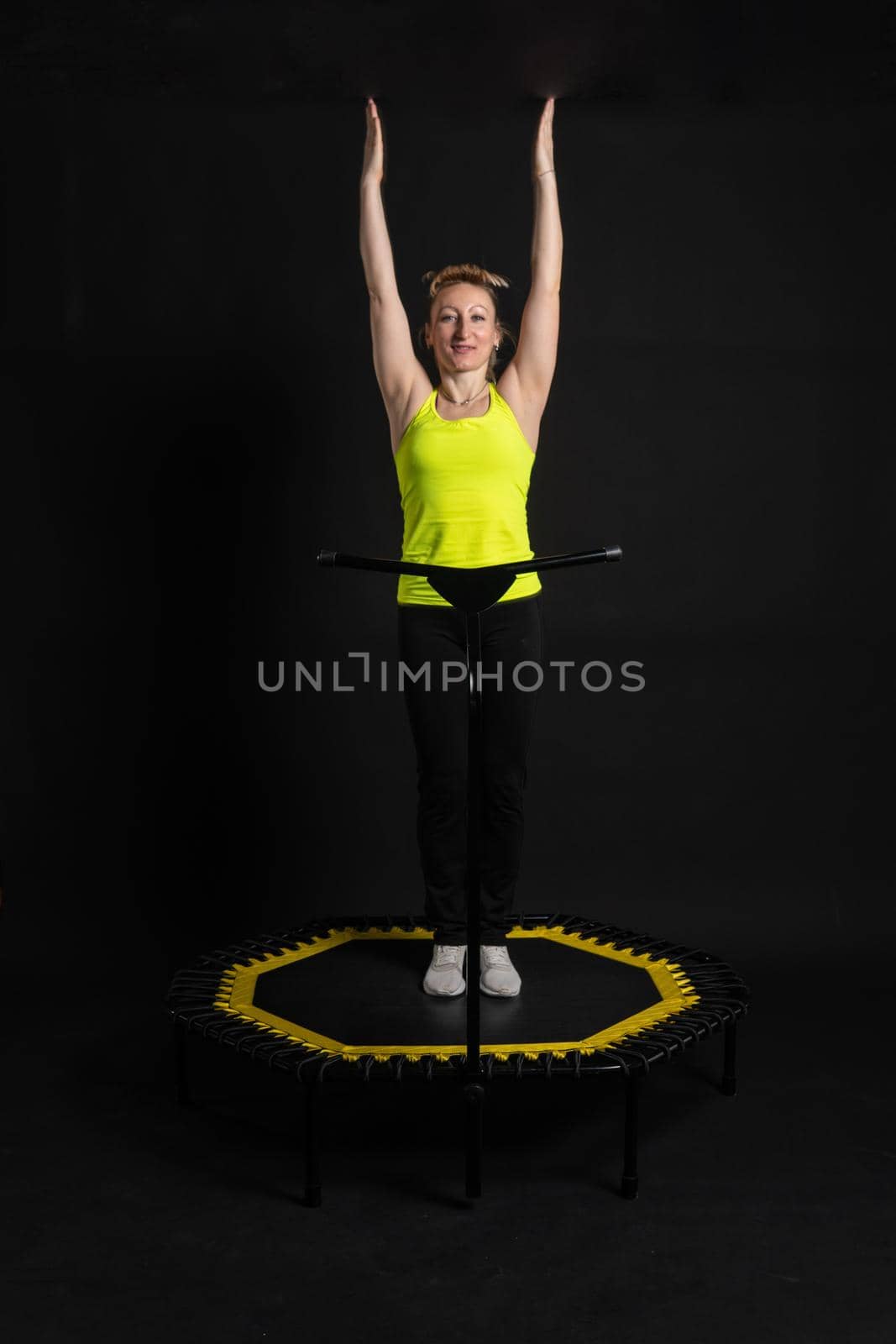 Girl on a fitness trampoline on a black background in a yellow t-shirt black energy woman, fun exercise caucasian health workout club. Wellness white athletic muscle instructor enjoy by 89167702191