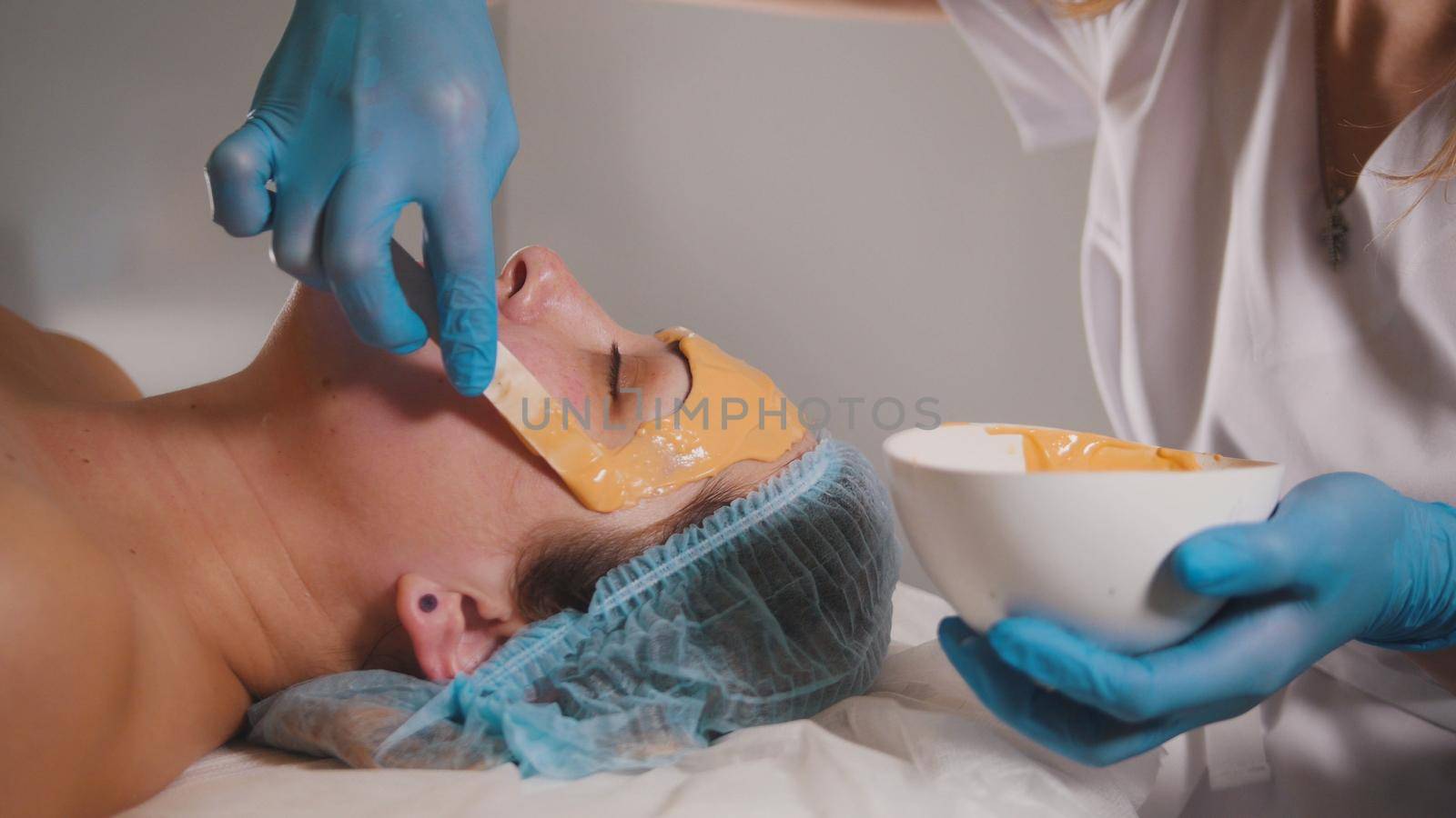 Close up of a person who visiting the beauty salon, fruit mask is applied on the face with a special wooden stick by Studia72