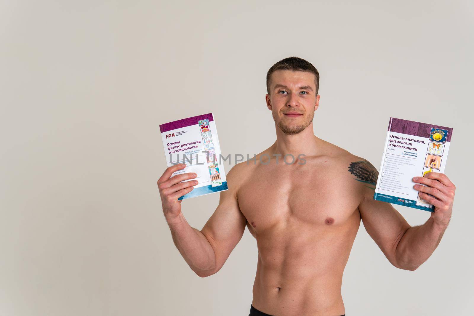 Bodybuilder reads the book on a white background isolated at the bottom of his head on his hands bodybuilder book macho, muscle fitness person chest intellectual Smile ABS gym, vision tan
