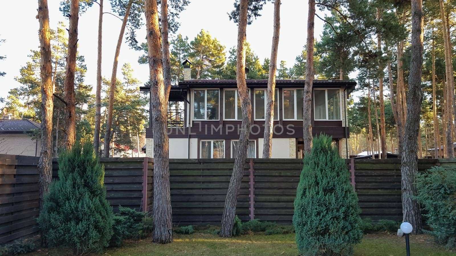 Large stylish and modern residential building and a huge courtyard with trees and flowers in a forest with sunbeams