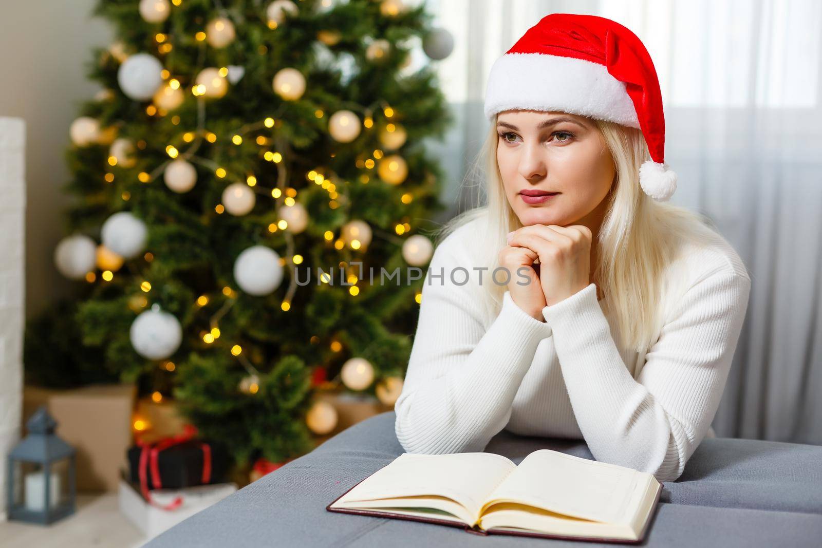 Beautiful young woman praying in front of the decorated Christmas tree