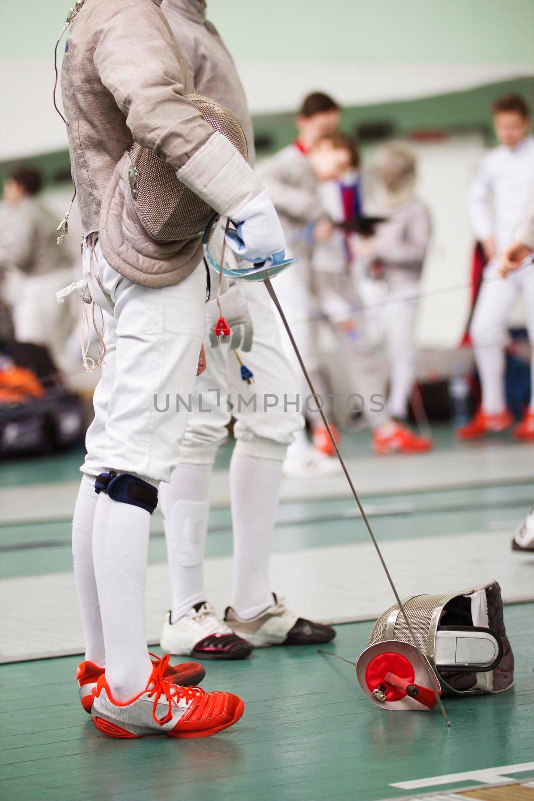 Fencer in white costume with rapier and protective mask on the floor in a fencing tournament, telephoto shot