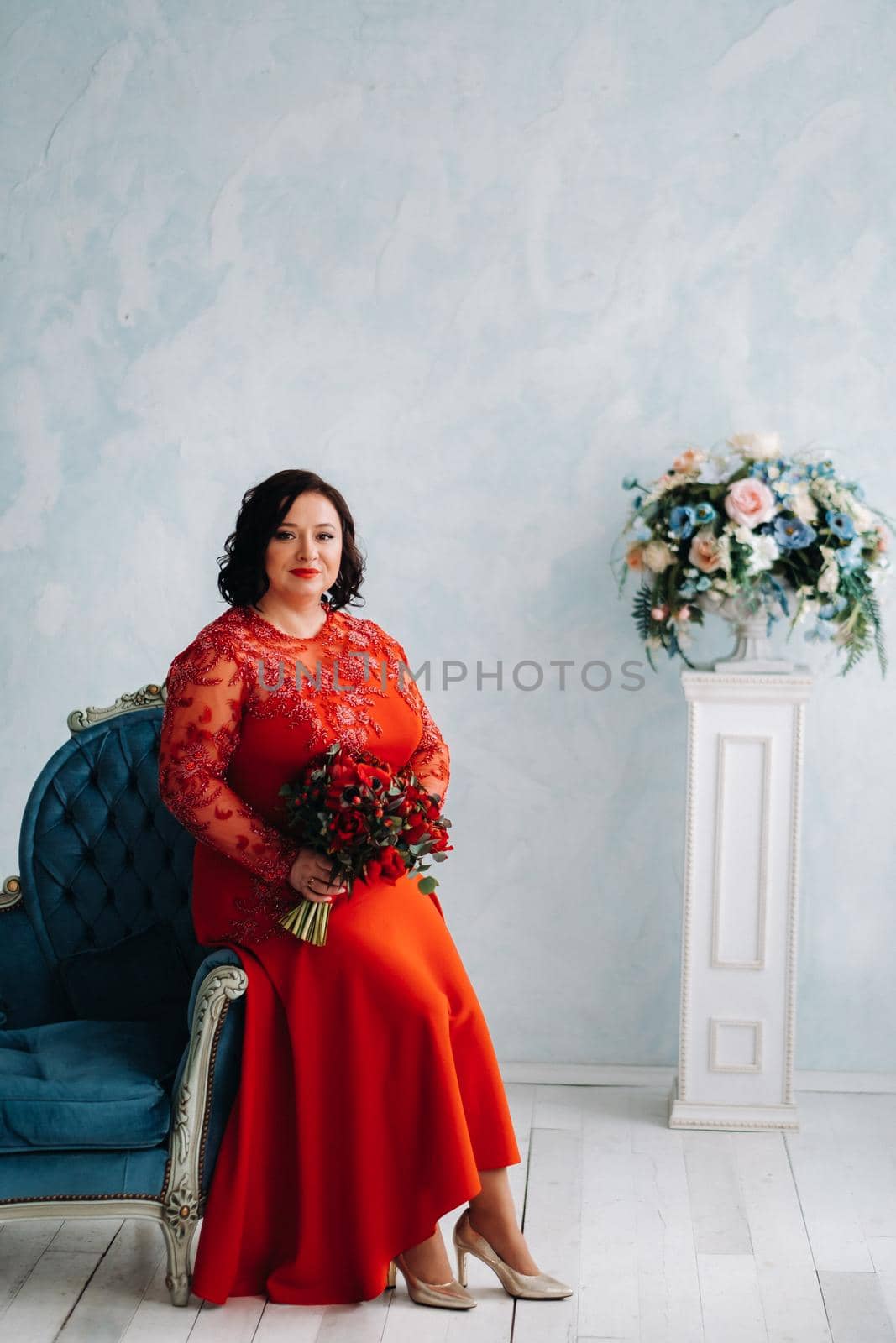 a woman in a red dress sits on a sofa and holds a bouquet of red roses and strawberries in the interior