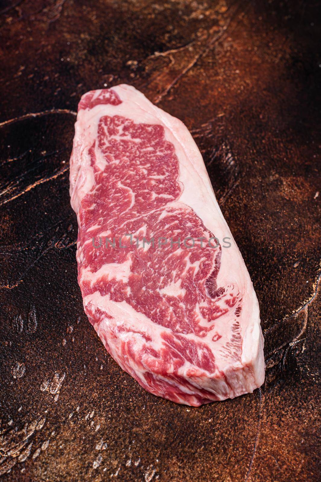 Raw new york strip steak or striploin on a butcher table. Dark background. Top view.