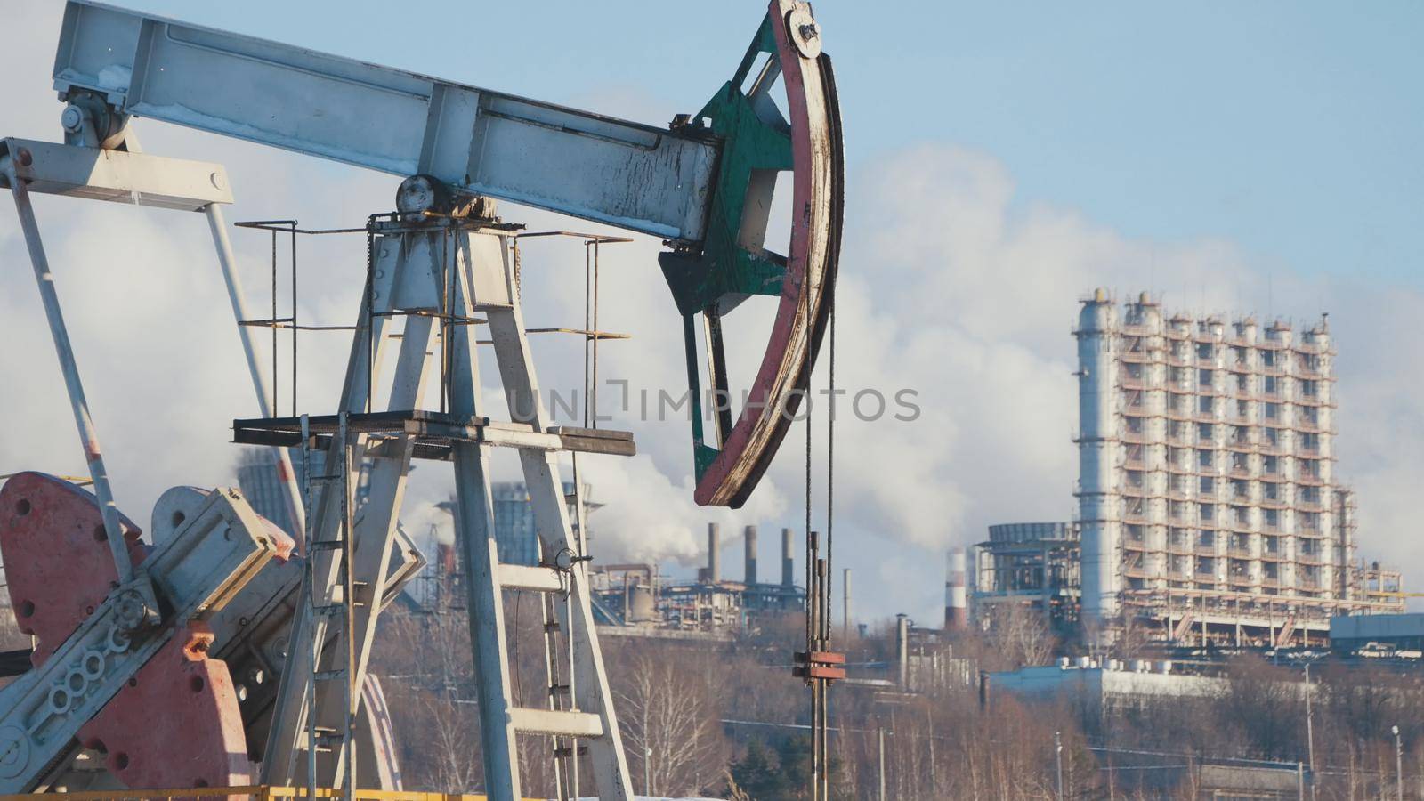 Close-up of a working pump for the extraction of crude oil and of a petrochemical plant's pipes emissions, petroleum industry