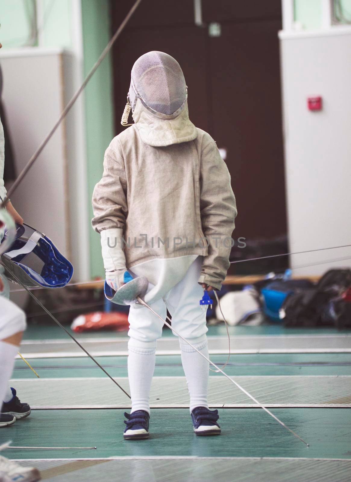 Young participant of the fencing tournament in white clothes and protective mask on the fencing tournament, telephoto shot