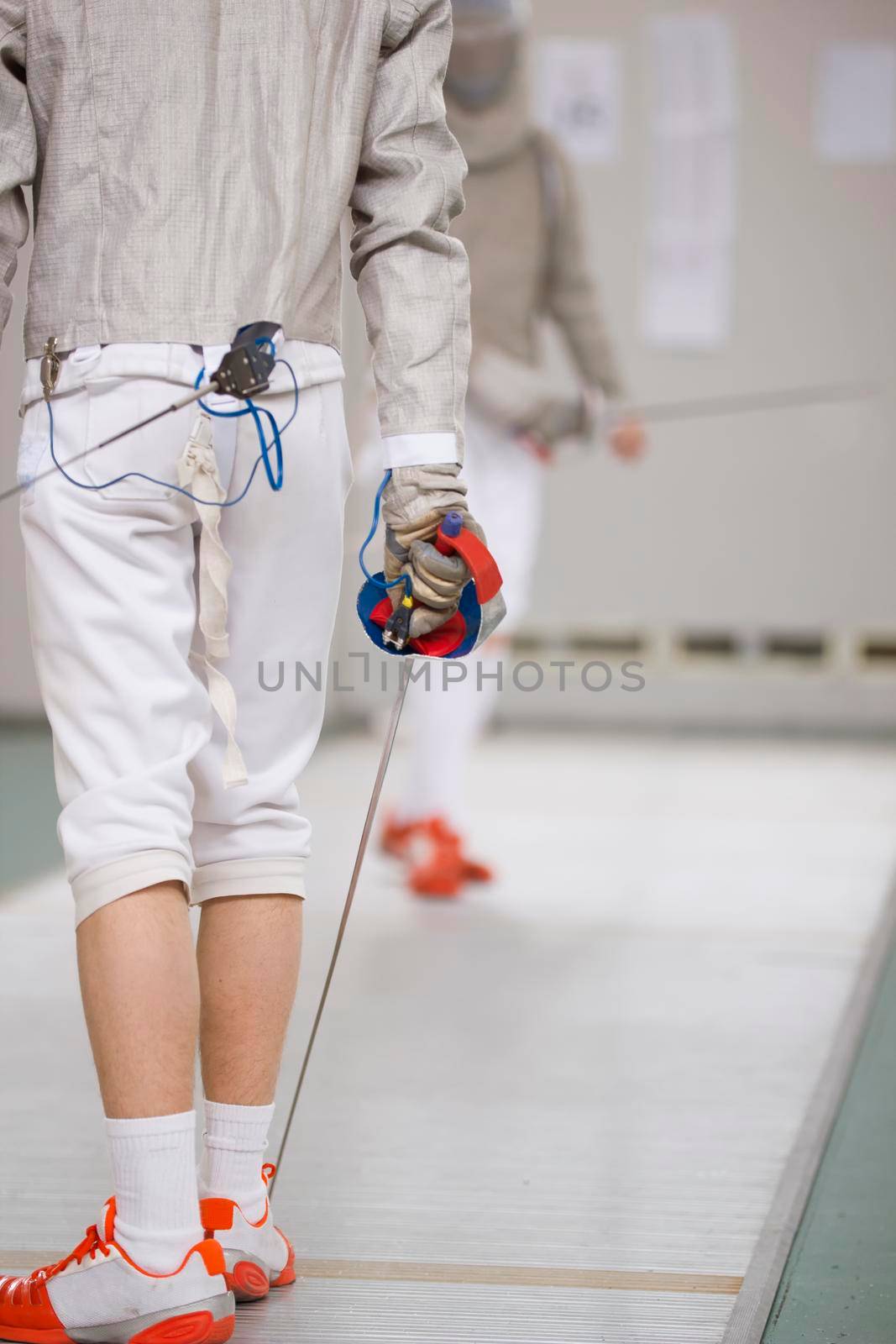 Rear view of teenage fencer in white clothes on the fencing tournament by Studia72