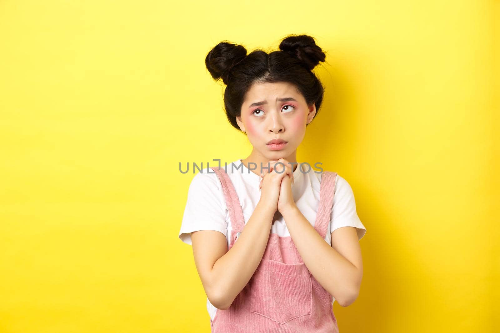 Sas asian girl holding hands in pray, pleading god, looking up and begging, standing on yellow background by Benzoix
