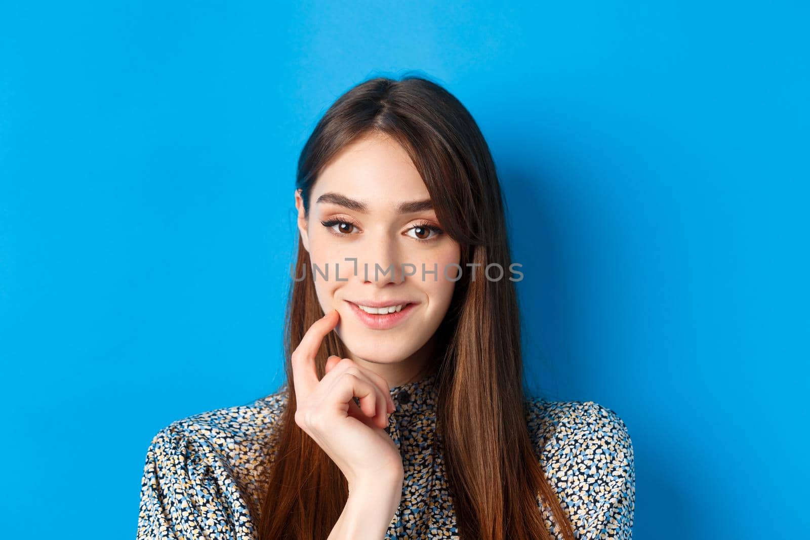 People emotions concept. Close-up portrait of intrigued pretty lady smiling and looking thoughtful, being interested, standing on blue background.