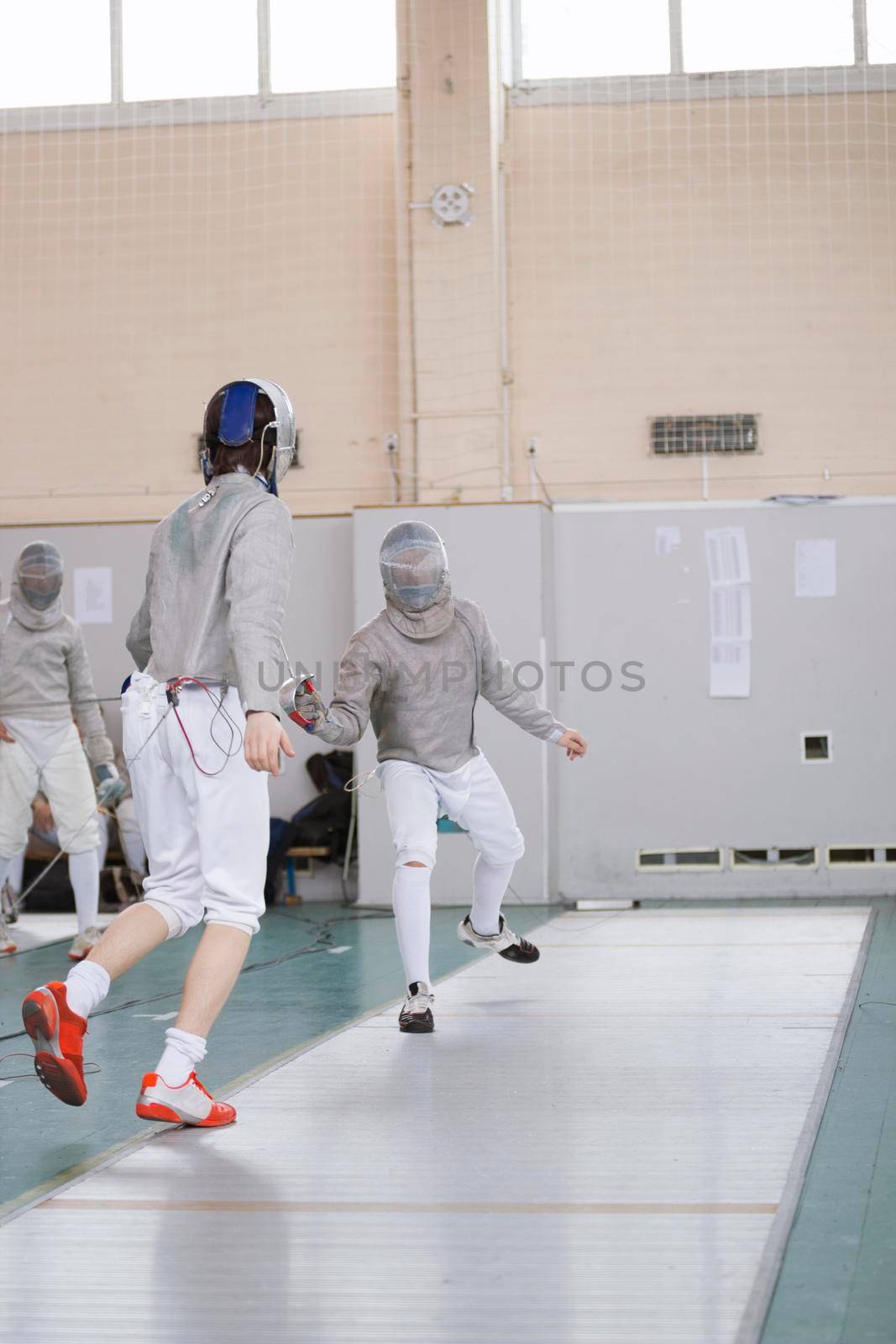 Young participants of the fencing tournament fighting in protective white clothes ,telephoto shot