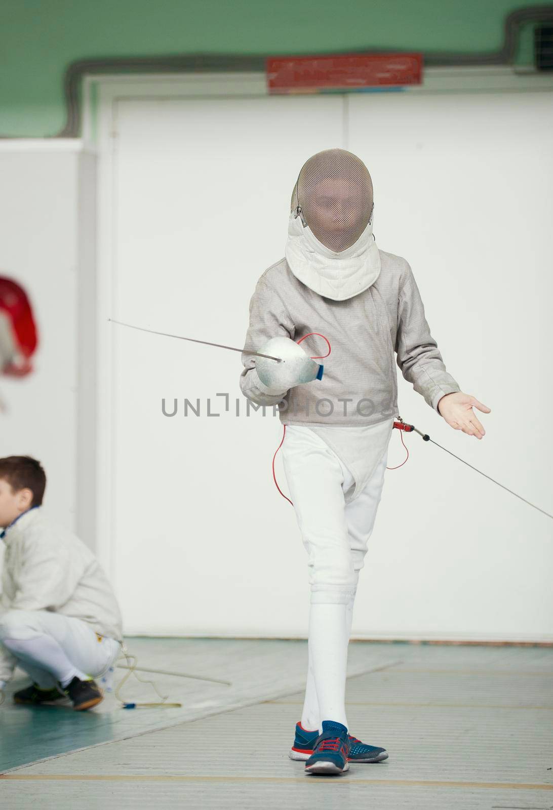 Boy teenager fencer in special costume at the fencing competition with rapier in fighting position, telephoto shot