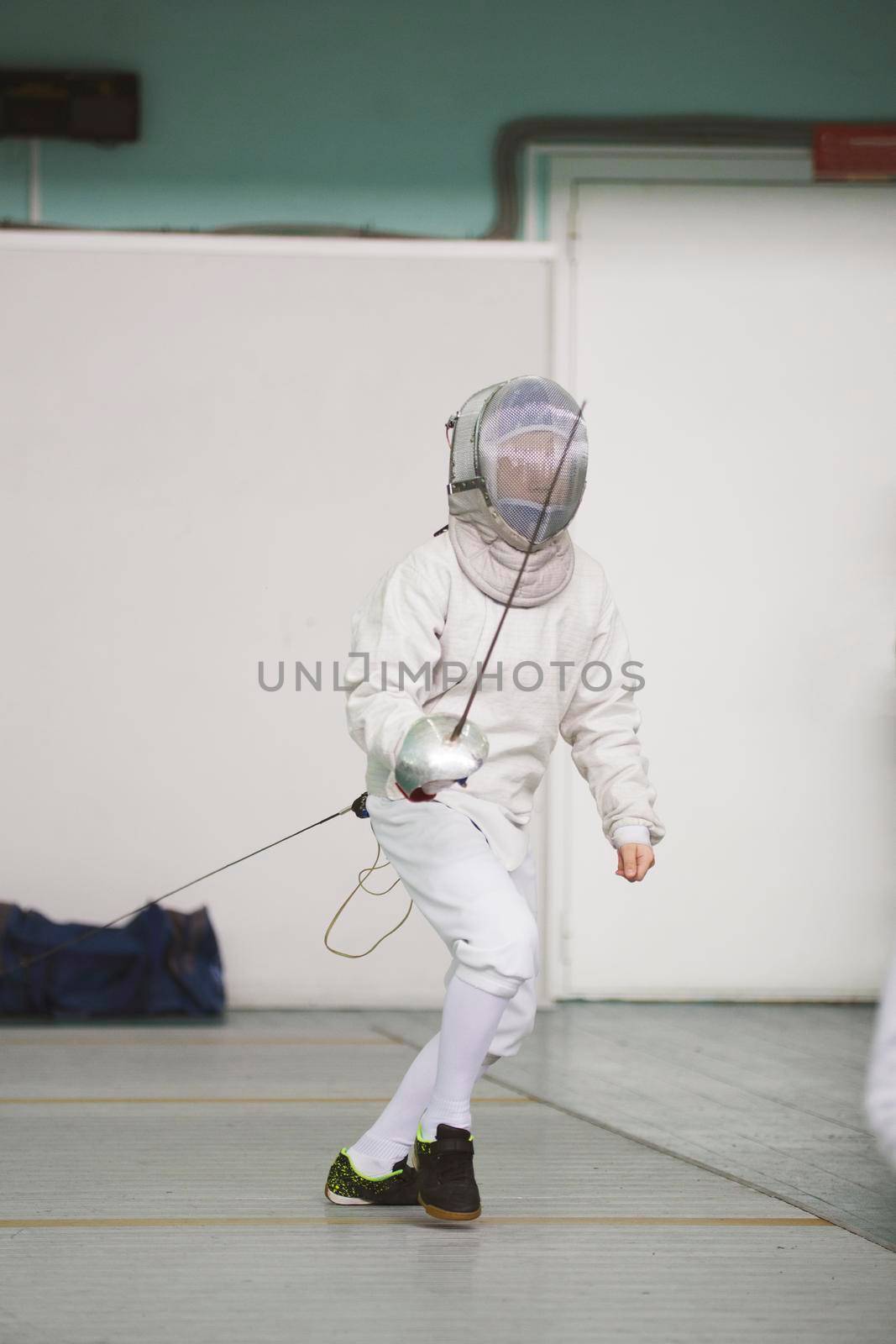 Boy teenager fencer in special costume at the fencing competition with rapier ready for fight, telephoto shot