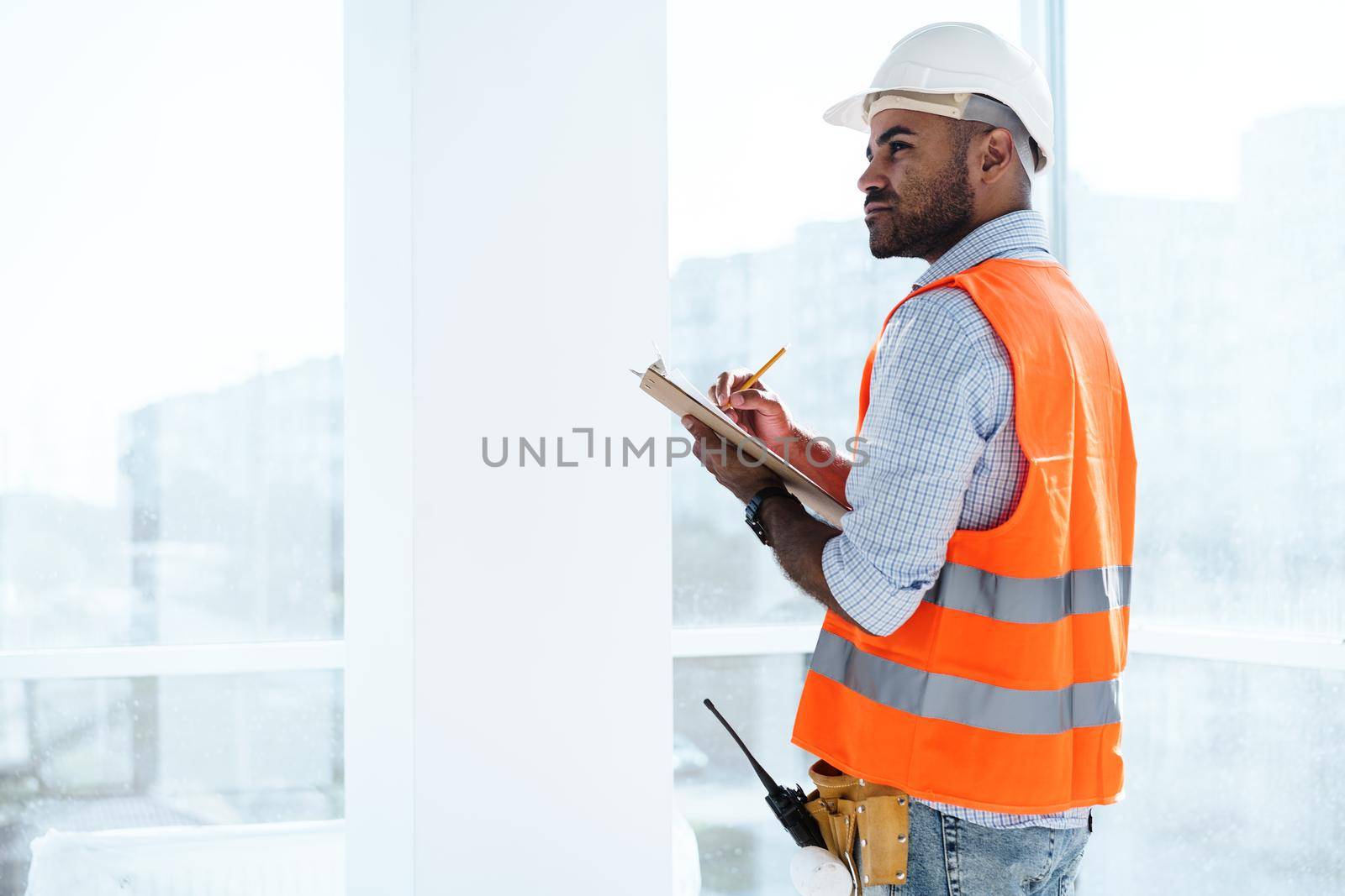 Foreman at work on construction site checking his notes on clipboard by Fabrikasimf