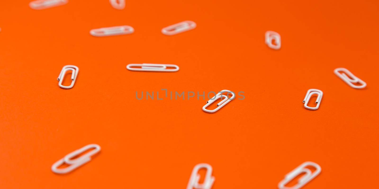 Close-up of white paper clips on a orange background. School stationery pattern