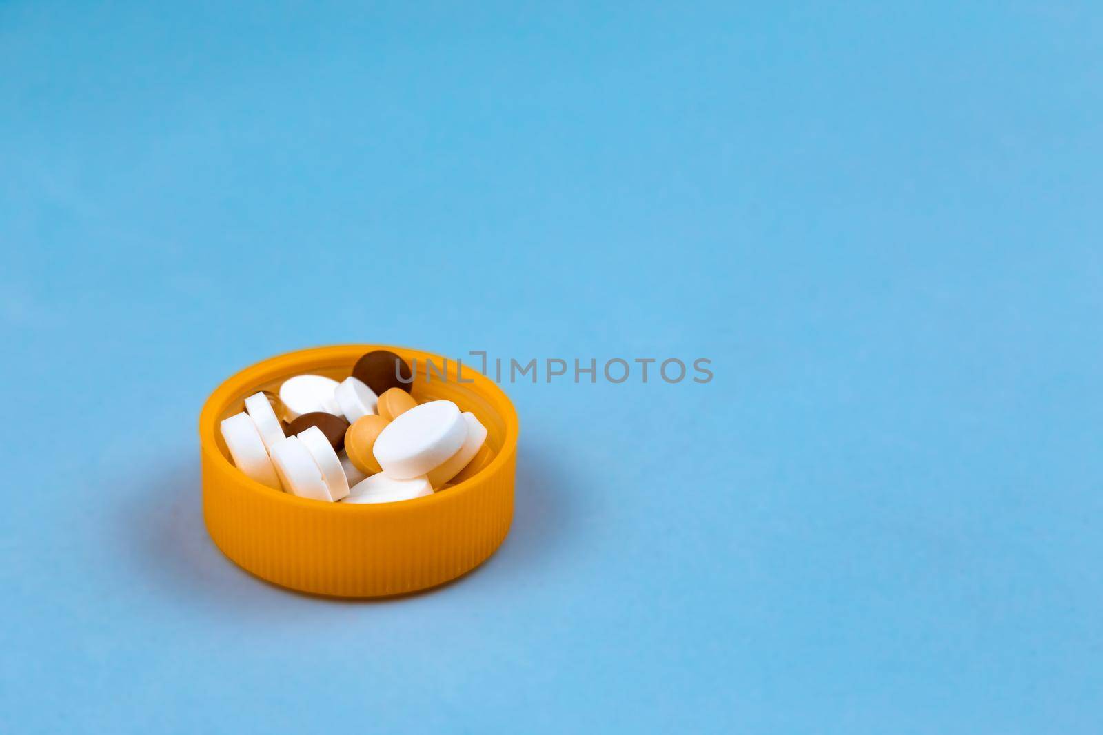 Dose of the colored pills in the cap of the package of pills. On blue background with copy space for text.