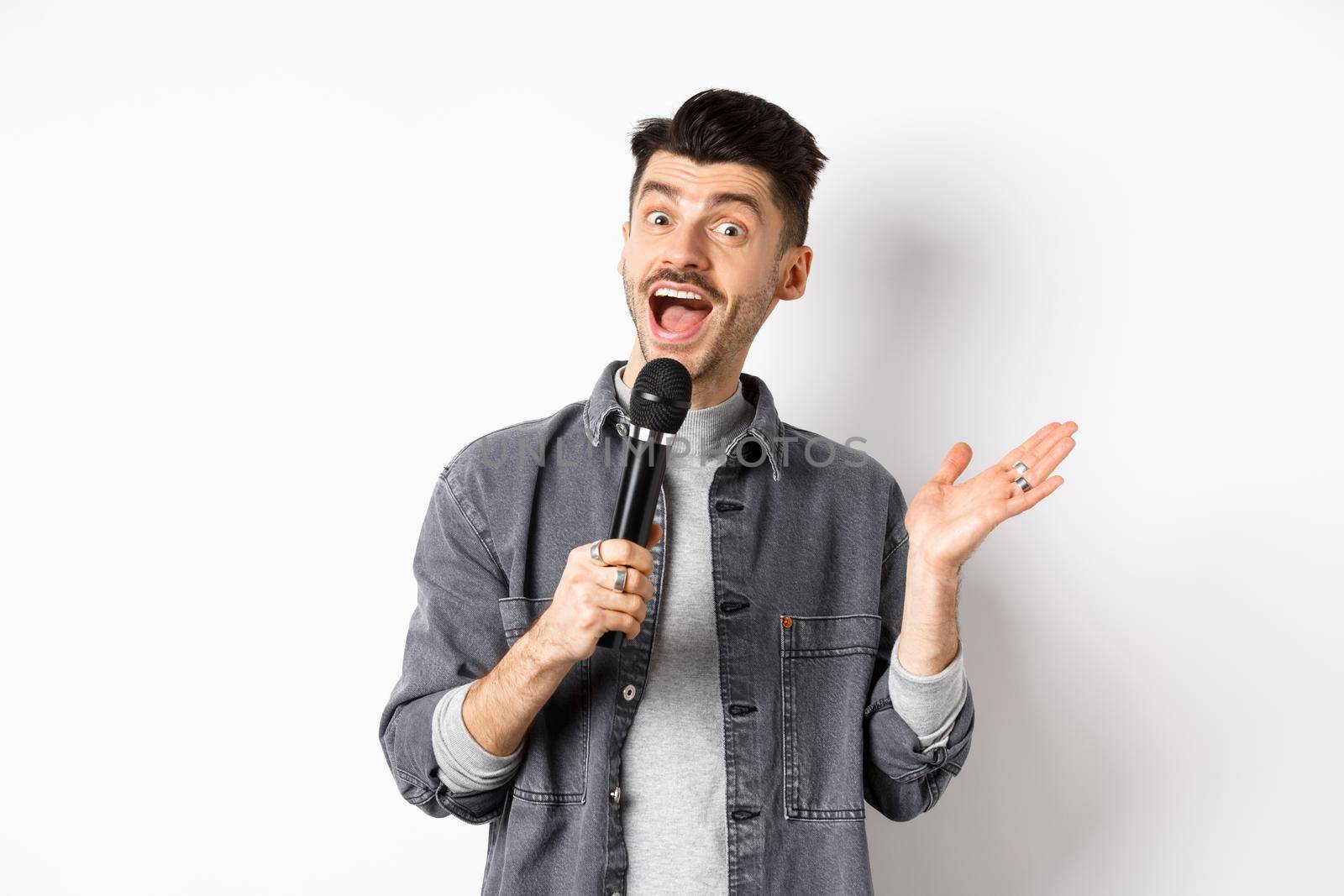 Excited stylish guy giving speech, talking in microphone, perform or sing karaoke, standing on white background by Benzoix