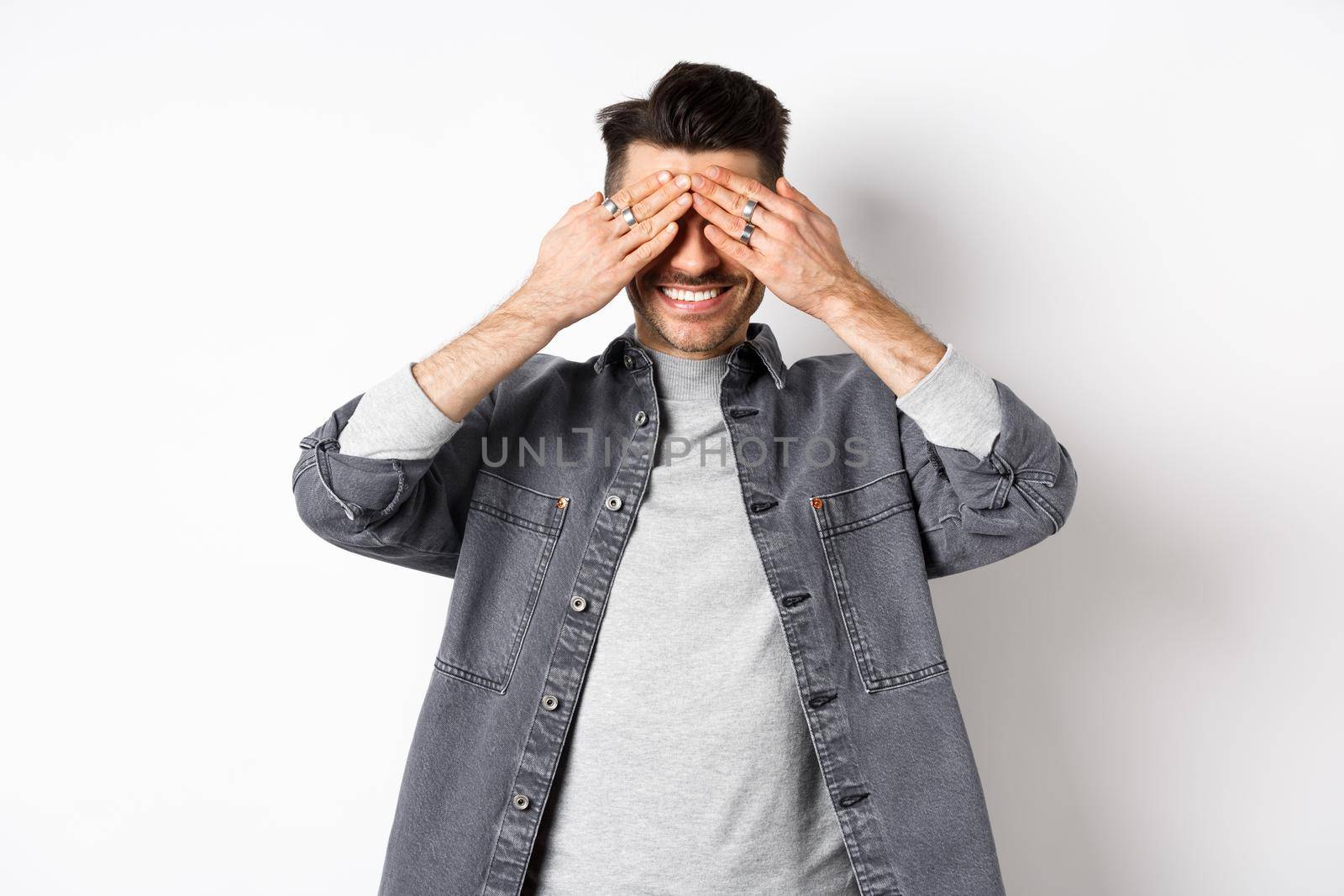 Happy smiling guy waiting with closed eyes for surprise, standing excited on white background.