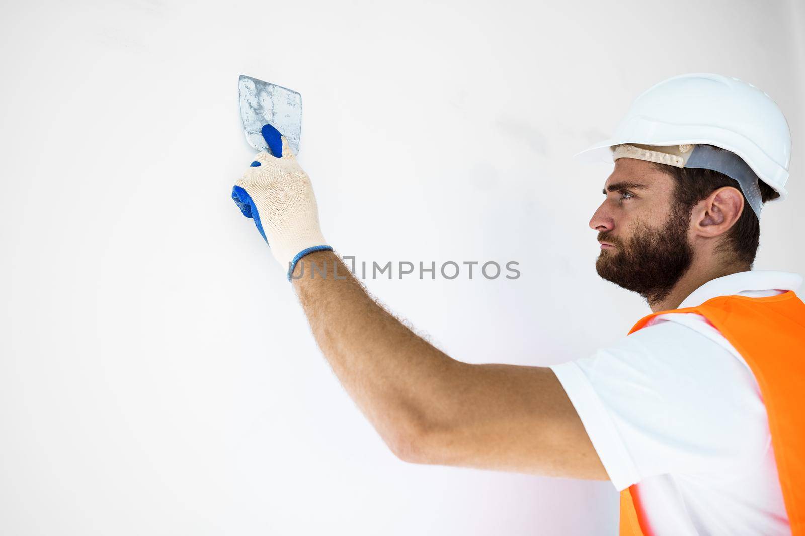 Plasterer in workwear smoothing wall surface of building indoors, close up